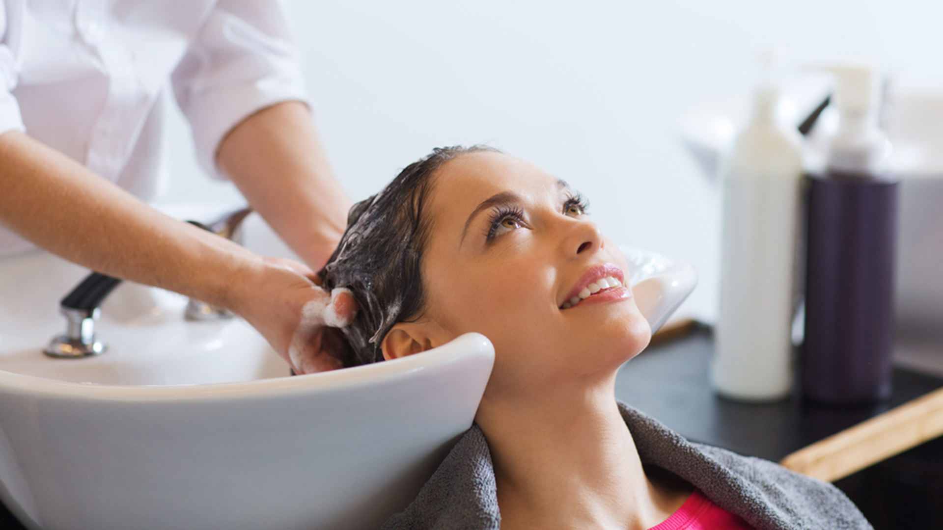 happy young woman with hairdresser washing head at hair salon